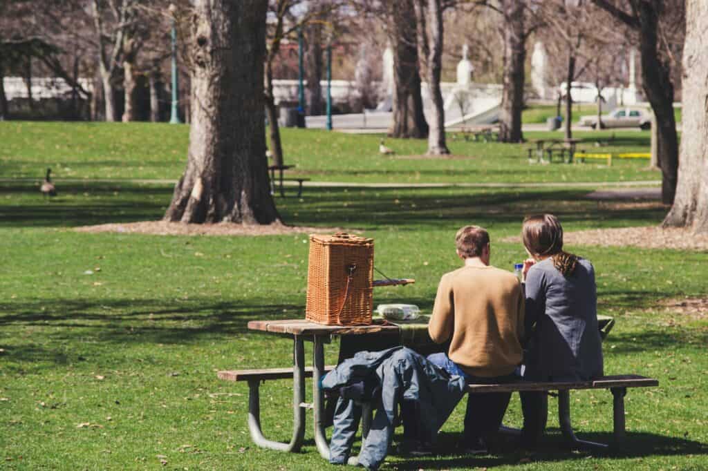 A couple is having a picnic in a park under the sun in the concept of parks and green spaces in Sutton.