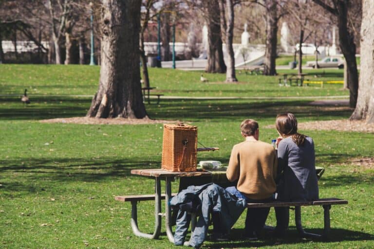 A couple is having a picnic in a park under the sun in the concept of parks and green spaces in Sutton.