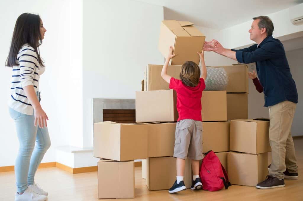 A father and children stacking cardboard in the concept of 'how to save money when moving to Sutton'.