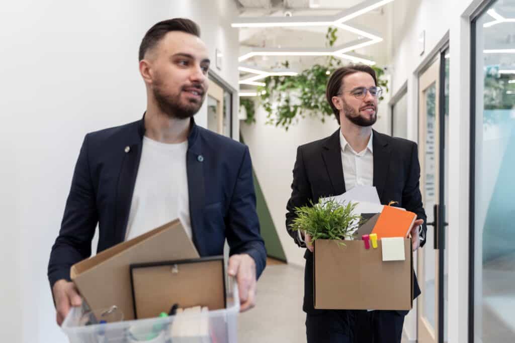 Two male employees carrying boxes containing some of their office items