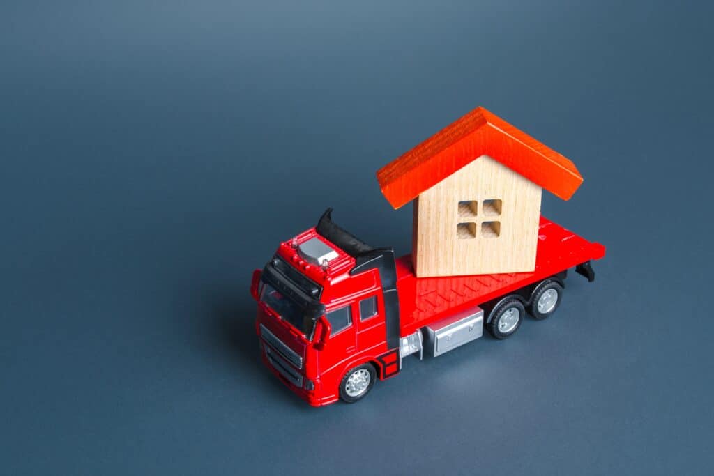A red toy truck carrying a wooden house figurine in the concept of home removals services